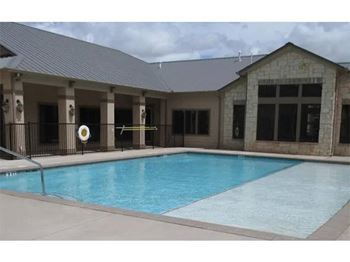 A pool in front of a building with a black fence.
